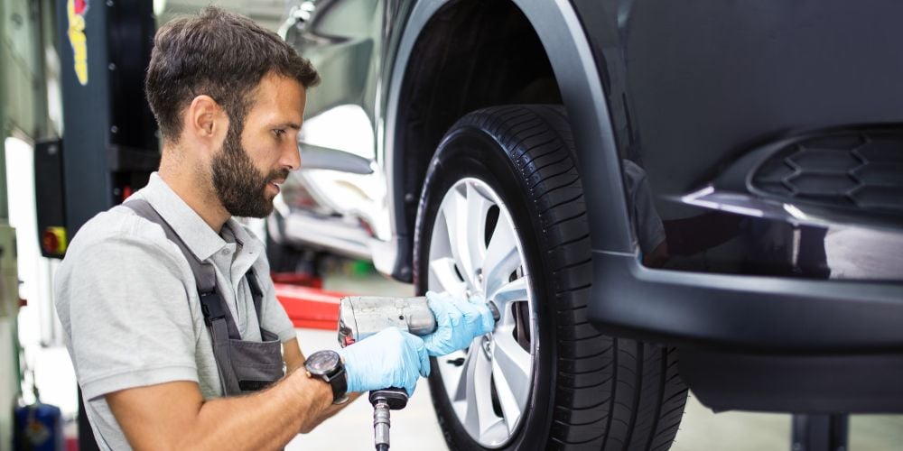 Mechanic using a pneumatic impact wrench to change a tire on an elevated car in an auto repair shop